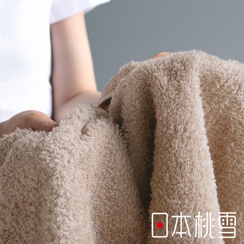 一隻手拿著一條淺棕色的毛巾，毛巾材質蓬鬆柔軟，上面有「日本桃雪」的標誌。