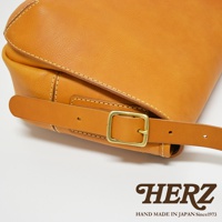 職人手作復古翻蓋郵差包，採用天然皮革製成，呈現溫潤的焦糖棕色。包款設有可調節的皮質背帶，配有黃銅色金屬針釦，展現經典工藝。