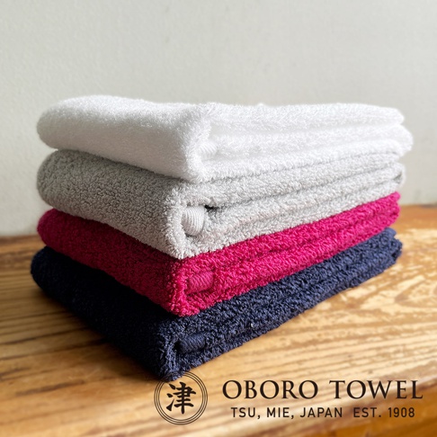 津OBORO品牌，百年之極摩登復古風細纖毛巾4入組，含白色、灰色、桃紅色及海軍藍，四色毛巾堆疊於木紋桌面。