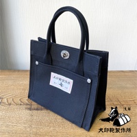 黑色純棉帆布迷你托特包，頂部有提把和旋轉鎖扣，正面有一個帶有品牌標籤的翻蓋口袋，口袋上裝飾有銀色鉚釘。