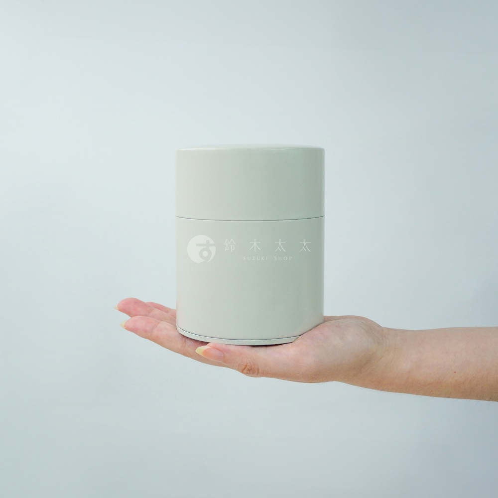 淺灰色圓柱形錫製茶葉罐，罐身上有白色「鈴木太太」和「SUZUKI SHOP」字樣及圖標，由一手托著。