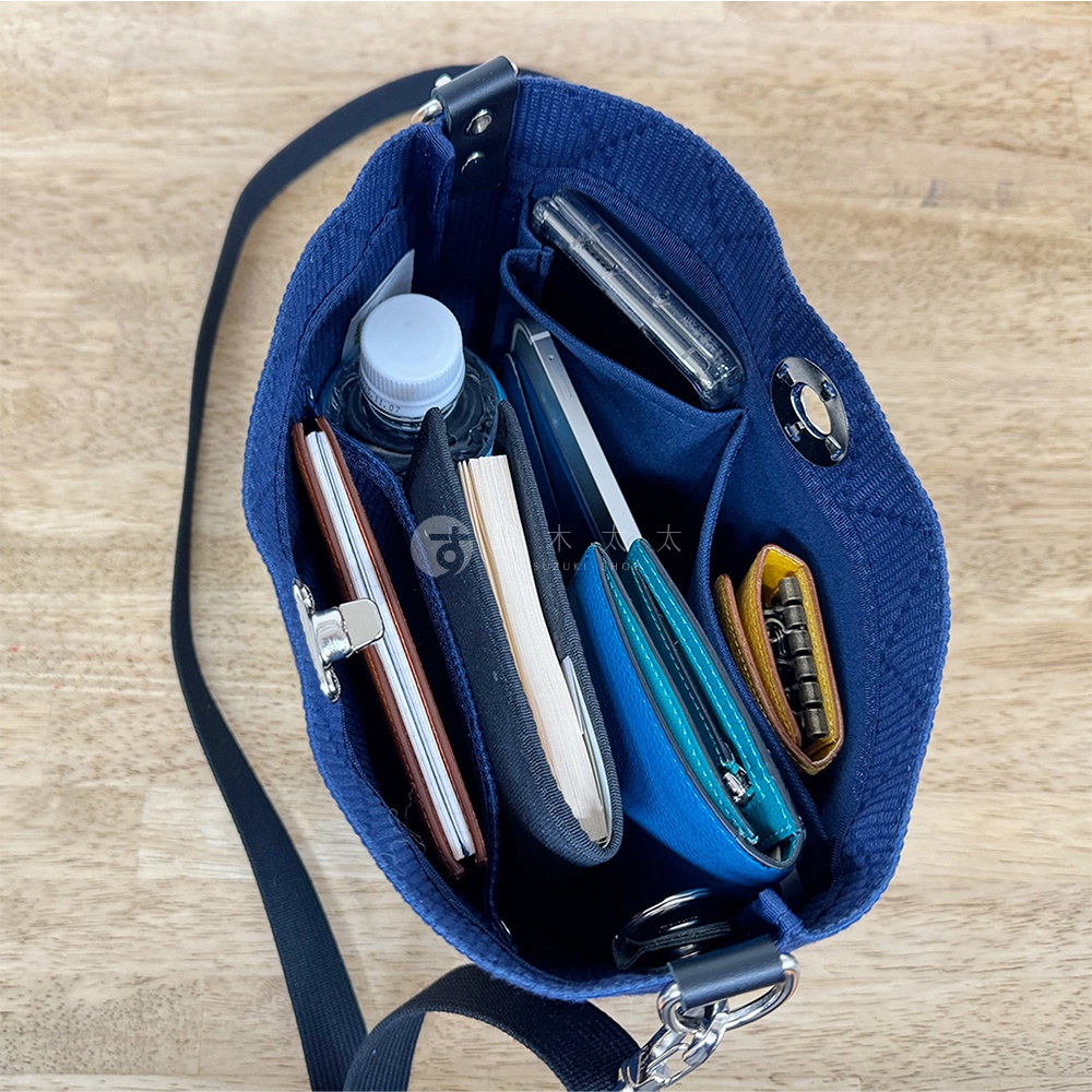 深藍色刺子織迷你側背包，內有手機、錢包、筆記本、水瓶和鑰匙包。