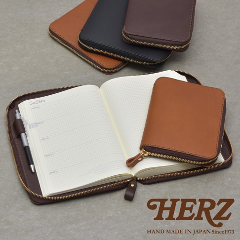 棕色皮革記事本收納包，搭配打開的筆記本，筆記本內頁有日期和方格，背景有黑色和深棕色收納包。