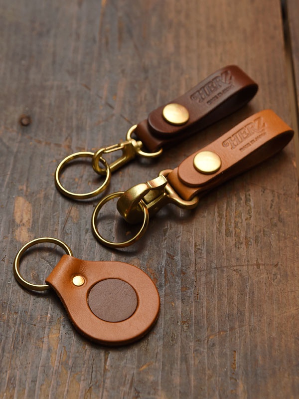 職人手作皮革鉤扣鑰匙圈，包含一個圓形棕色皮革鑰匙圈，以及兩個長方形皮革鑰匙圈，分別為棕色和淺棕色，皆配有黃銅色鉤扣和鑰匙圈。