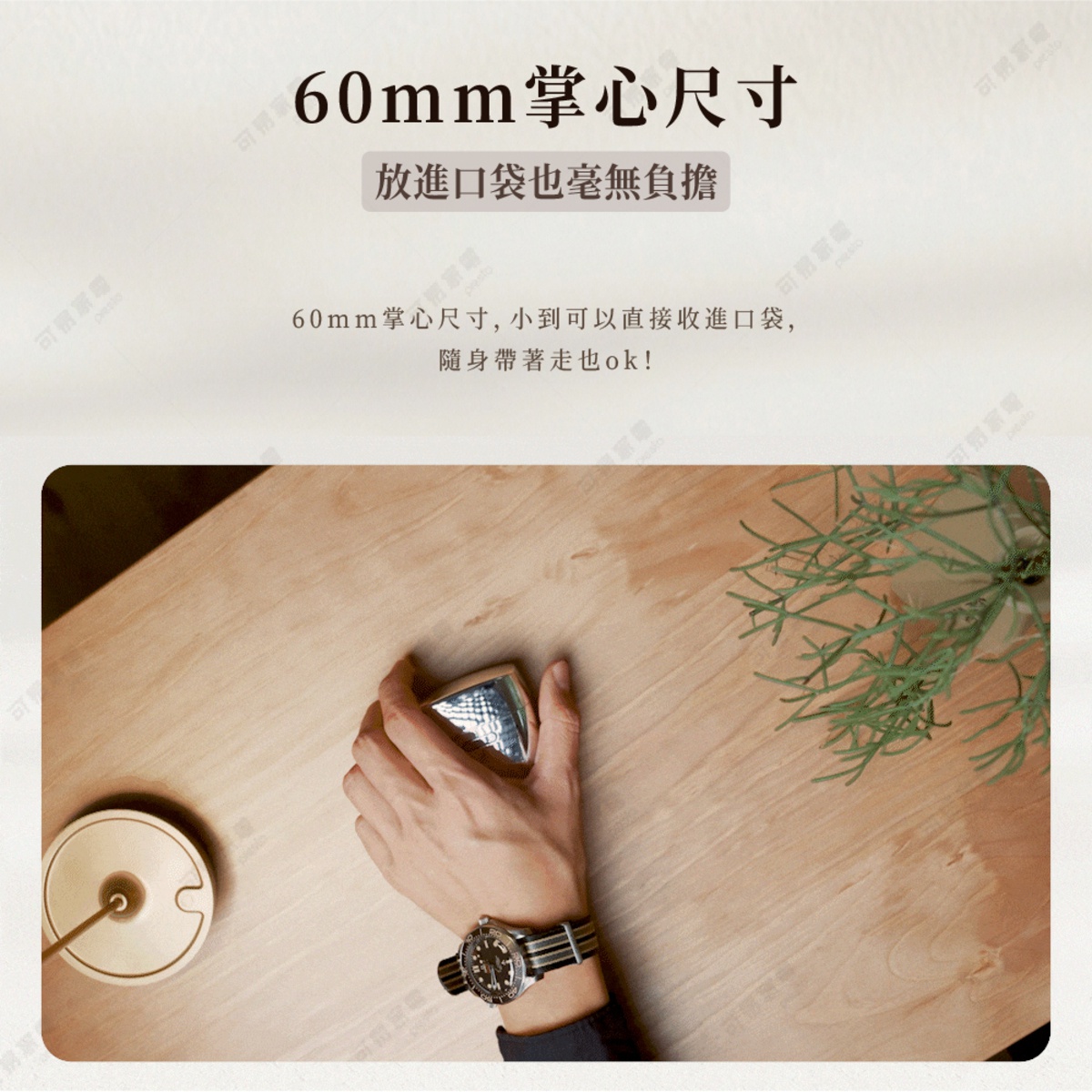從上方俯視的角度拍攝，一隻佩戴腕錶的手正覆蓋住一個精緻的金屬質感電動刮鬍刀，刮鬍刀尺寸約為六十毫米，顯得小巧便攜。背景為淺色木紋桌面，旁邊放置一個金色的圓形底座，畫面強調產品小巧且可輕鬆放入口袋隨身攜帶的特色。