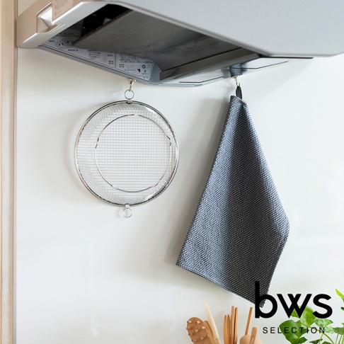 銀色不鏽鋼圓形淺型瀝水籃，網狀濾網設計，帶有掛環，懸掛於爐具下方，旁邊掛有一塊深灰色織紋毛巾。