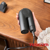 手持黑色摺疊吹風機，機身上有TESCOM品牌字樣，吹風機口有扇形網格，背景為木質桌面。