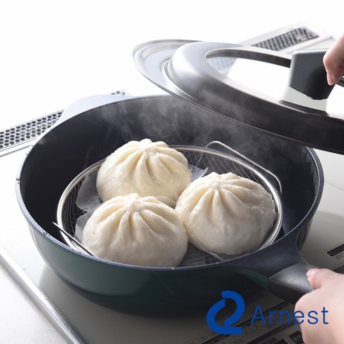 一個人手持鍋蓋正在打開一個深綠色的平底鍋，鍋內放著金屬蒸網架，上面擺放著三顆蒸好的熱氣騰騰白色包子，下方印有 Arnest 品牌標誌。