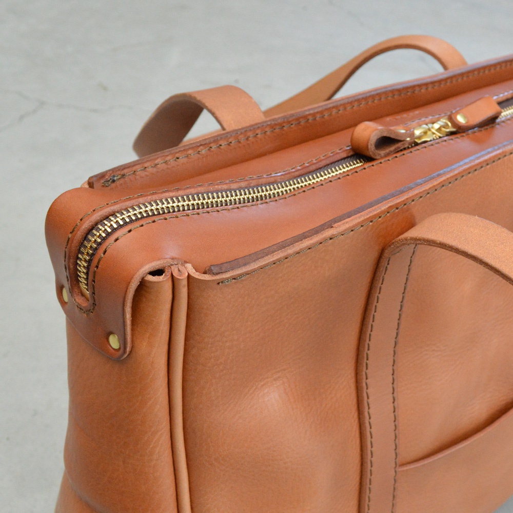 職人手作皮革Organ肩背拉鍊托特包，採用棕褐色皮革，配有金色拉鍊和皮革提把，包款結構紮實，車縫線清晰。