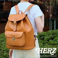 職人手作經典皮革後背包，採用溫暖的淺棕色皮革，設有翻蓋抽繩主袋及前置小口袋，以精緻的縫線點綴，呈現自然質樸的風格。