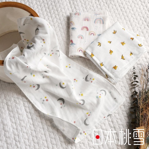 模式B： 一條印有月亮和星星圖案的白色紗布毛巾，一旁疊放著兩條印有彩虹和黃色小果實圖案的方巾，背景為白色格紋織物，右側有乾燥花束裝飾，右下角有「日本桃雪」字樣。