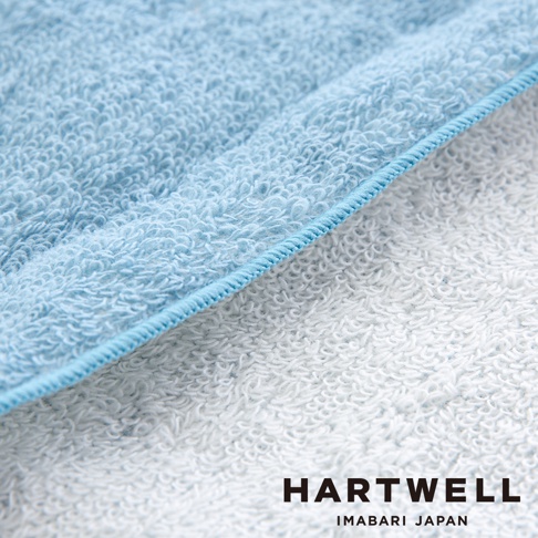 淺藍色與白色毛巾布料特寫，展示細緻柔軟的毛圈質地，以及藍色滾邊縫線，品牌標誌 HARTWELL IMABARI JAPAN 位於右下方。