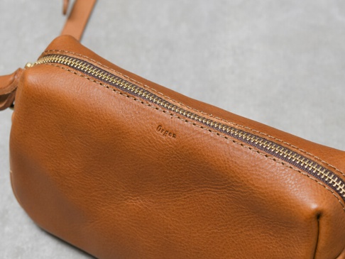 職人手作的棕色皮革單肩包，設有精緻的黃銅拉鍊和壓印的「Organ」字樣，皮革表面帶有自然的紋理。