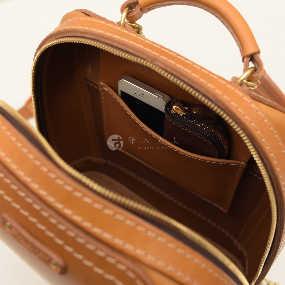 職人手作皮革立體商務後背包 R-3，展現棕褐色牛皮材質與手工縫線細節。內部空間可見手機與零錢包，設計簡潔實用。