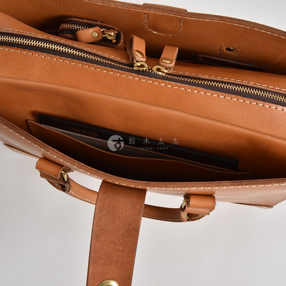 職人手作皮革三層收納兩用商務公事包，呈現溫潤的棕褐色調。包款內部結構清晰，可見拉鍊開合、皮革內袋及細緻的縫線，展現高品質工藝。