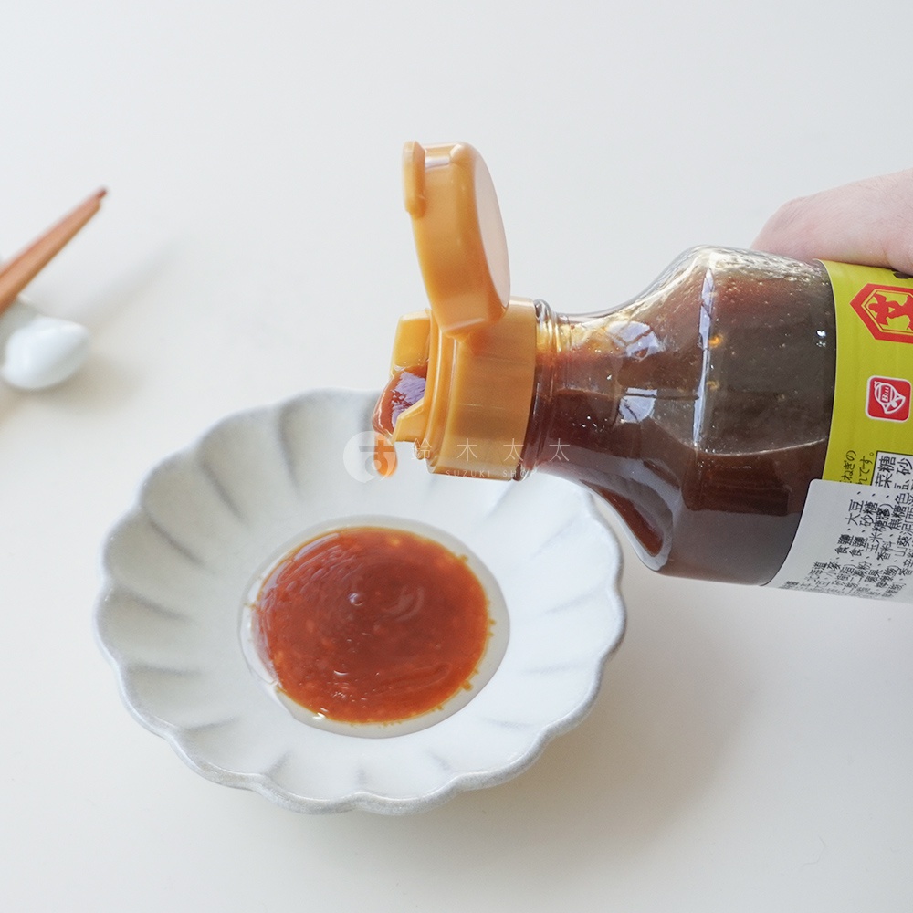 一瓶醬料瓶傾斜，將深褐色的醬料滴入一個扇形的小碟子中，小碟子裡的醬料呈現紅褐色。