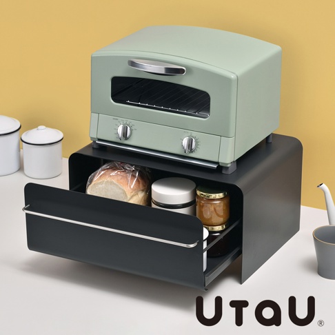 淺綠色復古烤箱置於黑色抽屜式收納櫃上方，收納櫃內有麵包、罐子和果醬。