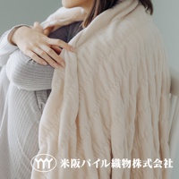 米色輕暖柔蓬抗摩四季毯，觸感柔軟，表面有菱格紋理，蓋在身穿灰色條紋衣物的女性身上。