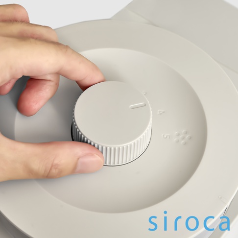 淺灰色 SC-C2510 石臼式全自動研磨咖啡機，特寫鏡頭顯示手指正在轉動淺灰色的旋鈕，旋鈕上有刻度標示，旁邊有數字「4」、「5」及咖啡豆圖示。