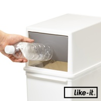 一只手正將一個透明塑膠瓶放入白色垃圾桶的灰色推蓋開口。