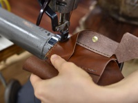 手工縫製的棕色皮革三折式迷你短夾，細節處有黃銅按鈕，展示製作過程。