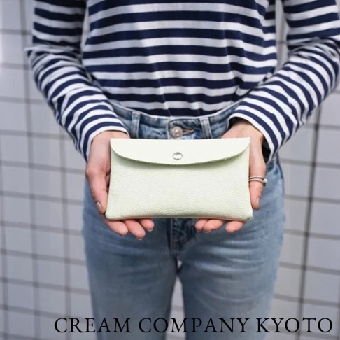 淺綠色皮革多功能收納包，帶有銀色按扣，質地略有紋理，由雙手持握。