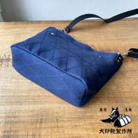 深藍色刺子織迷你側背包，表面有菱格紋縫線，附有黑色織帶和金屬扣環。