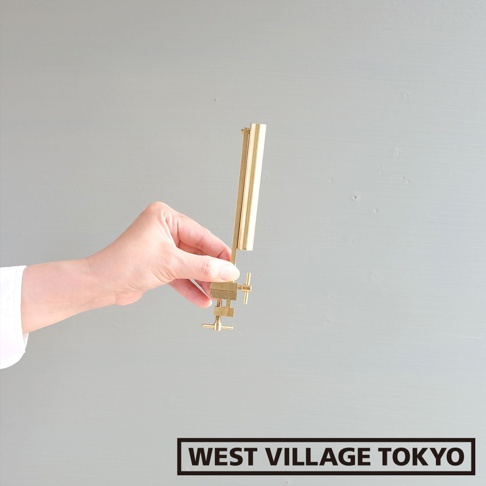 手持黃銅金屬花器，花器為圓筒形，帶有可夾式底座，底座上有兩個旋鈕，整體呈現金屬原色。