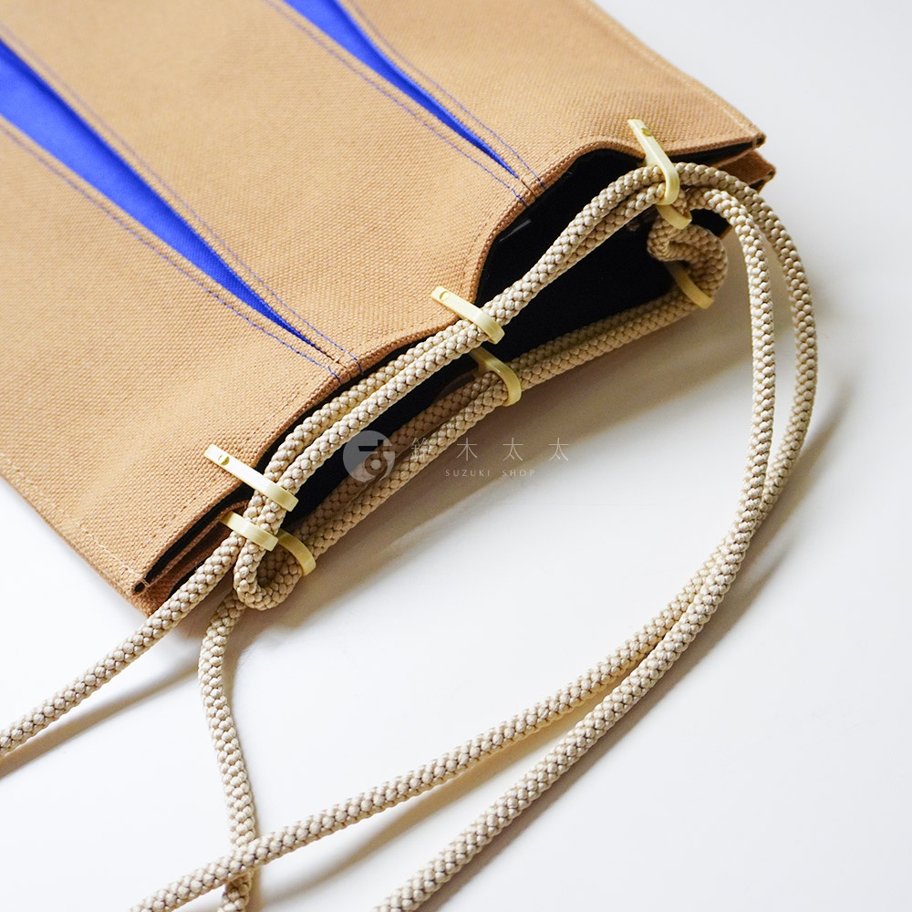 這是一個京都KOSHO品牌的ougi帆布信玄袋，特寫展示了棕色帆布材質與藍色內襯的細節，以及透過淺色塑料扣環穿過編織繩索所形成的束口設計，繩索自然垂落，整體呈現出簡約的日式風格。