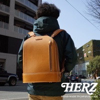 職人手作淺棕色皮革立體商務後背包，具有簡潔的方形輪廓，正面中央有一條垂直拉鍊，搭配對比色的縫線，展現細緻工藝。