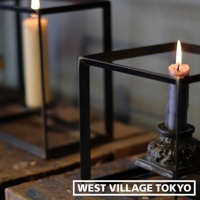 兩個鐵製長方展示架，其中一個架上放置著一支燃燒中的淡粉色蠟燭，另一架內有支米白色蠟燭，背景模糊。