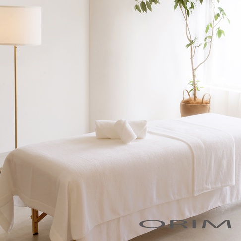 潔白的輕羽恆柔耐久輕質毯覆蓋在按摩床上，上面疊放著兩條白色毛巾。