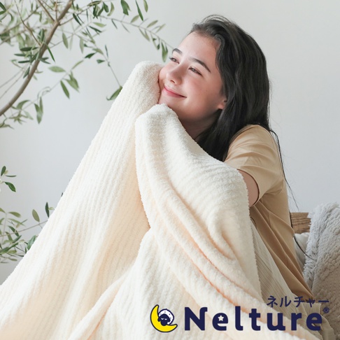 一位年輕女子被奶油色柔軟毛毯包裹，毛毯有著細緻的條紋織紋。