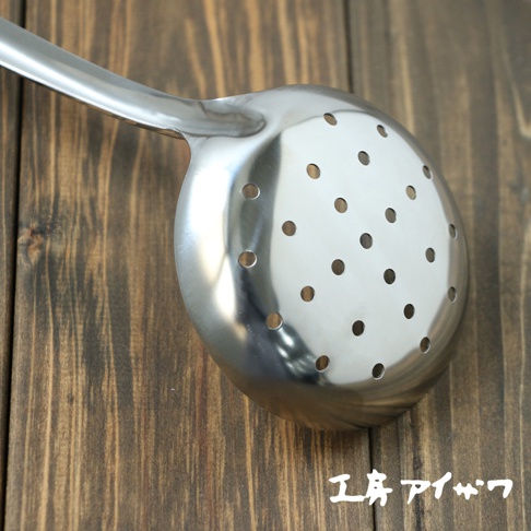 一個不鏽鋼中型撈勺，勺面帶有許多圓形孔洞，勺柄光滑，置於木紋背景上。