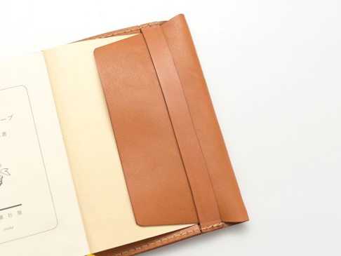 棕褐色皮革翻蓋記事本書套，左側露出部分泛黃內頁，書套有縫線細節。
