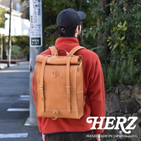 一個身穿紅色刷毛外套的人背著一個棕色皮革後背包，背包採用捲口設計，並配有可調節皮帶和金屬扣環。