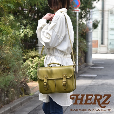 職人手作的綠色皮革單肩包，採用經典箱型設計，配有雙皮帶與金屬扣環，可肩背或手提，展現商務休閒風格。