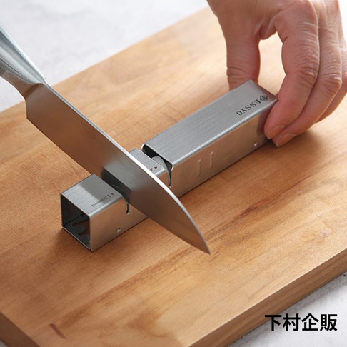 ESSYO 越匠系列可拆式不鏽鋼雙滾輪磨刀器，銀色不鏽鋼材質，搭配木質砧板，展示刀刃置於磨刀器中。