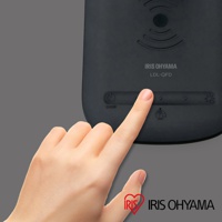 黑色Qi無線充電盤檯燈LDL-QFD，表面印有「IRIS OHYAMA LDL-QFD」字樣，並有觸控按鈕與指示燈。一只手的手指正按下其中一個按鈕。