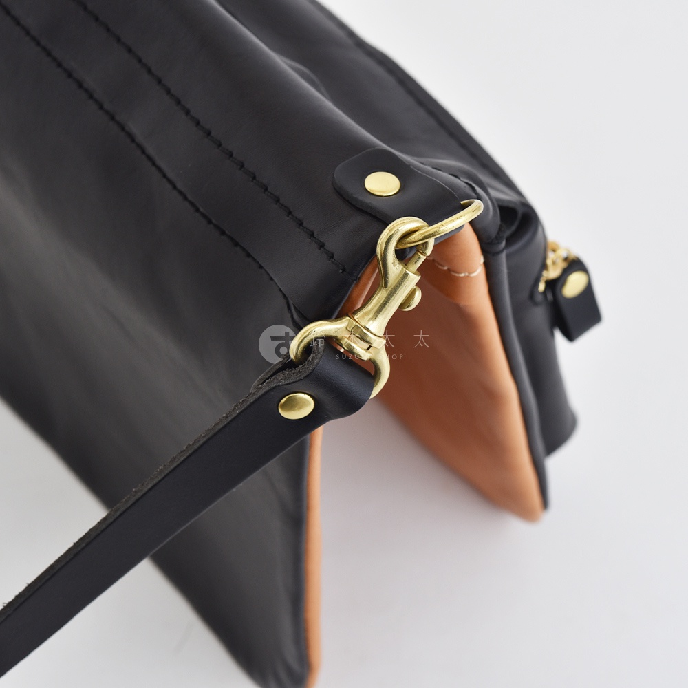 黑色皮革翻轉雙色直式斜背包，搭配黃銅金屬扣環和揹帶，內裡為棕色皮革。