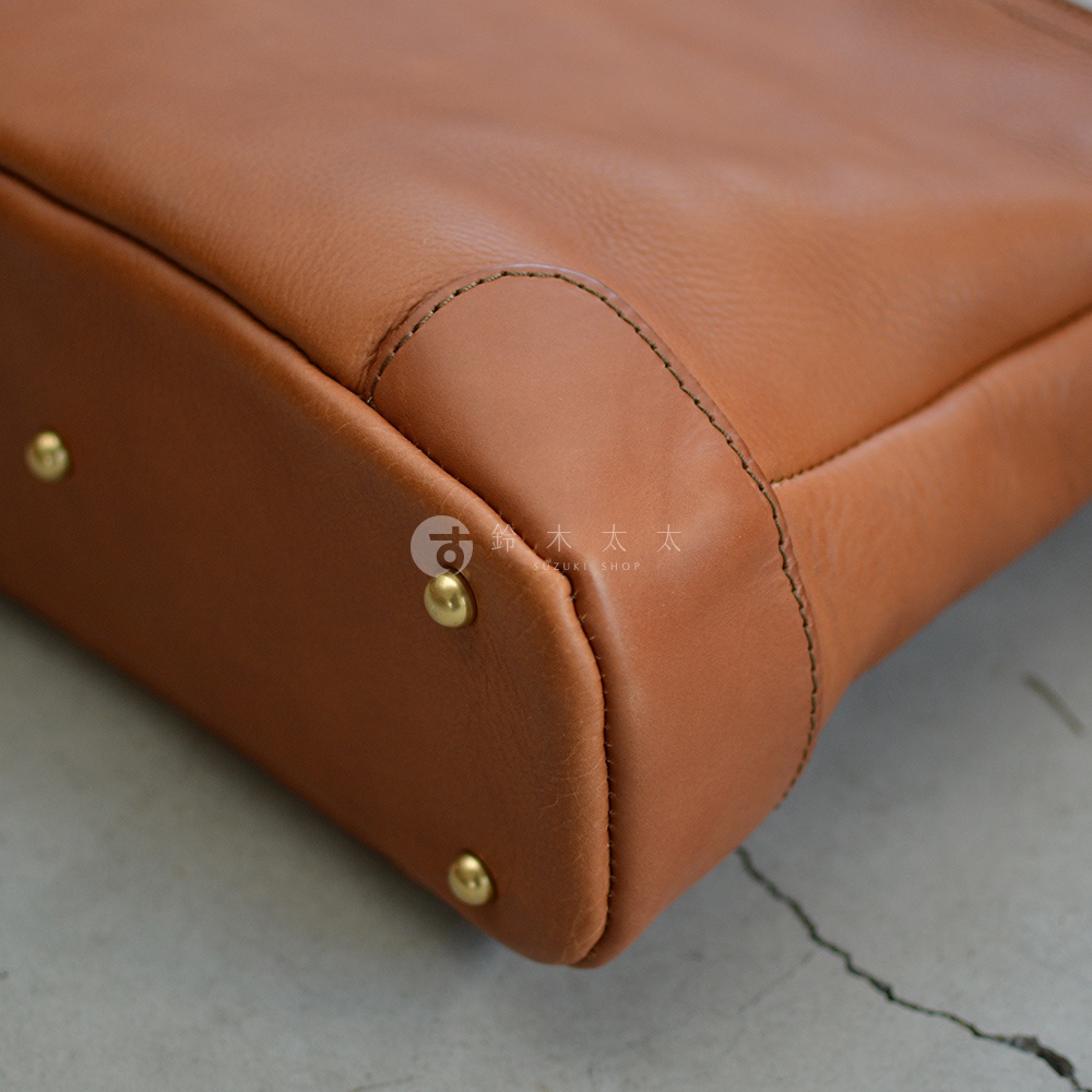 職人手作皮革Organ兩用商務托特包，採用溫潤的棕色皮革，包身邊角處縫線工整，並有金色卯釘裝飾。