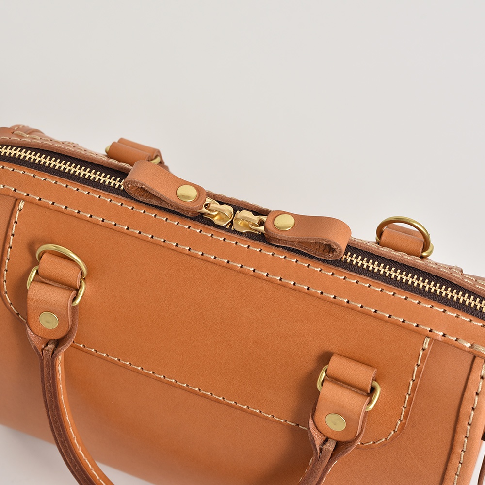 職人手作皮革迷你波士頓包，採用天然棕色皮革，搭配金色金屬拉鍊及五金配件，車縫線清晰，展現細膩質感。