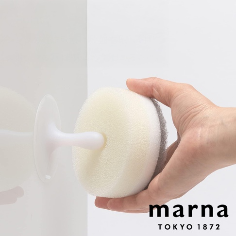 marna POCO 附吸盤洗碗海綿，由人手握持，展示其圓形海綿和背面的灰色清潔墊，吸盤固定在白色牆面上