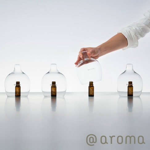 四個透明玻璃瓶，每個瓶內各有一個棕色小玻璃瓶裝的精油，其中一個玻璃瓶由一隻手持起，露出瓶內的精油。