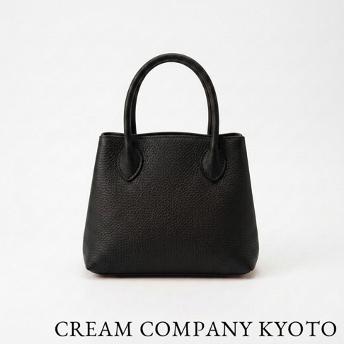 這是一款由 CREAM COMPANY KYOTO 出品的極簡風格黑色皮革手提托特包，採用紋理細膩的牛皮材質製成，外型簡約洗練，正下方印有品牌名稱字樣。