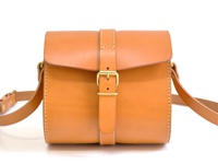 職人手作的棕色皮革皮扣單肩包，配有可調節皮帶和黃銅色金屬扣環，簡約設計，適合日常攜帶。