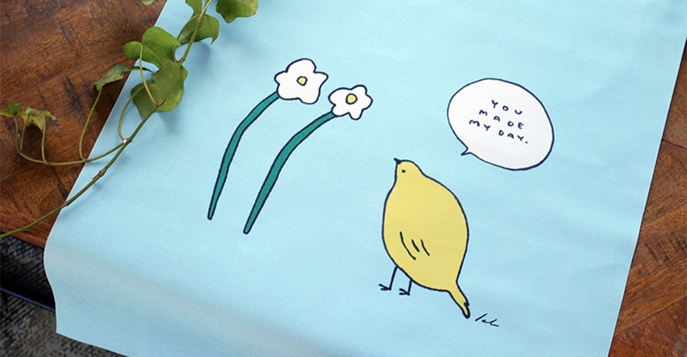 淺藍色帆布上印有手繪風格的可愛圖案：一隻黃色小鳥、兩朵白色小花，以及一個寫著「YOU MADE MY DAY.」的對話框。