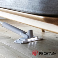 淺灰色電動平板拖把，配有LED照明，正在清潔木質地板下方的空間，拖把頭採用白色布墊。