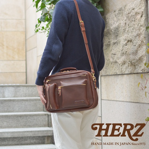 職人手作的深棕色皮革多功能收納單肩包，配有頂部提把、可拆卸肩帶，正面有三個拉鍊口袋和一個附加的開放式口袋，包身線條簡潔，皮革質感良好。