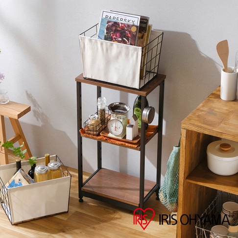 三層窄型鐵木層架，黑色鐵架搭配木紋層板，頂層放置黑色網籃，內有雜誌與米白色布襯。